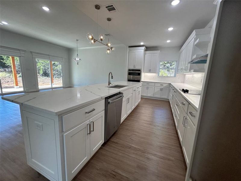 Kitchen with sink, pendant lighting, stainless steel dishwasher, white cabinets, and a center island with sink