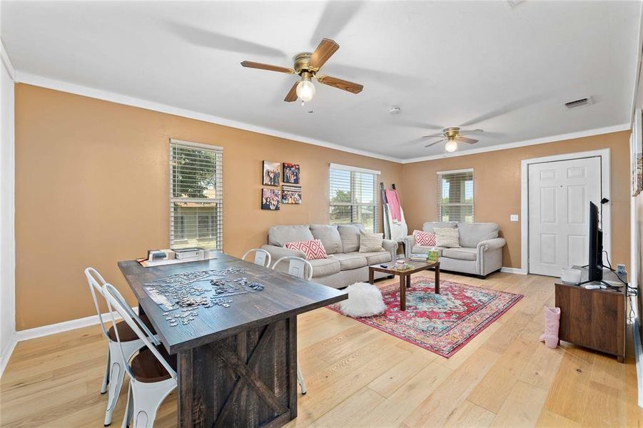 Living room featuring ceiling fan, crown molding, and light wood-style flooring Living room featuring ceiling fan, crown molding, and light wood-style flooring