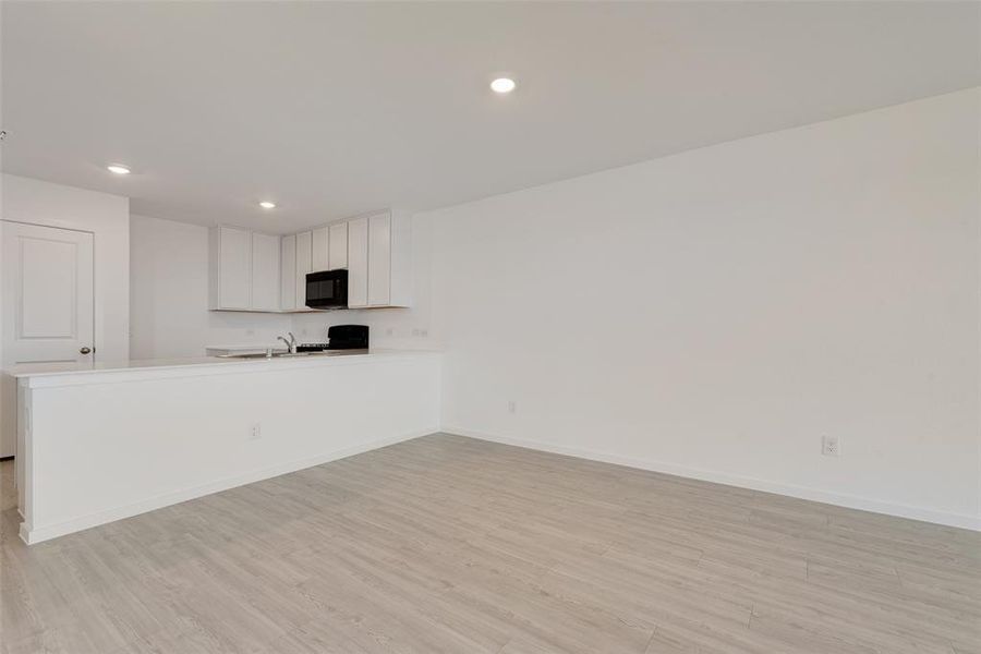 Kitchen with kitchen peninsula, light hardwood / wood-style flooring, white cabinets, and range