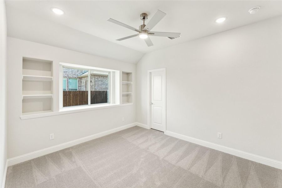 Empty bedroom with vaulted ceiling, ceiling fan, built-in shelves, and carpet flooring
