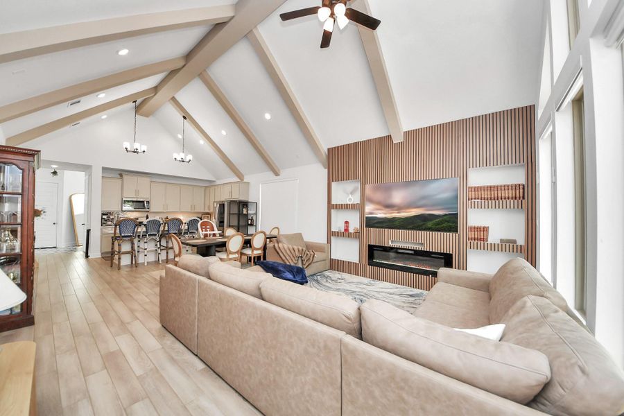 This spacious open-concept living area features high vaulted ceilings with exposed beams, a cozy modern fireplace, and abundant natural light from large windows. The kitchen offers ample cabinetry and a large island, perfect for entertaining. This spacious open-concept living area features high vaulted ceilings with exposed beams, a cozy modern fireplace, and abundant natural light from large windows. The kitchen offers ample cabinetry and a large island, perfect for entertaining.