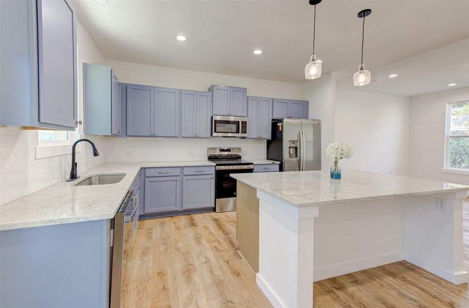 Kitchen featuring light stone counters, stainless steel appliances, decorative light fixtures, a center island, and light wood-style floors