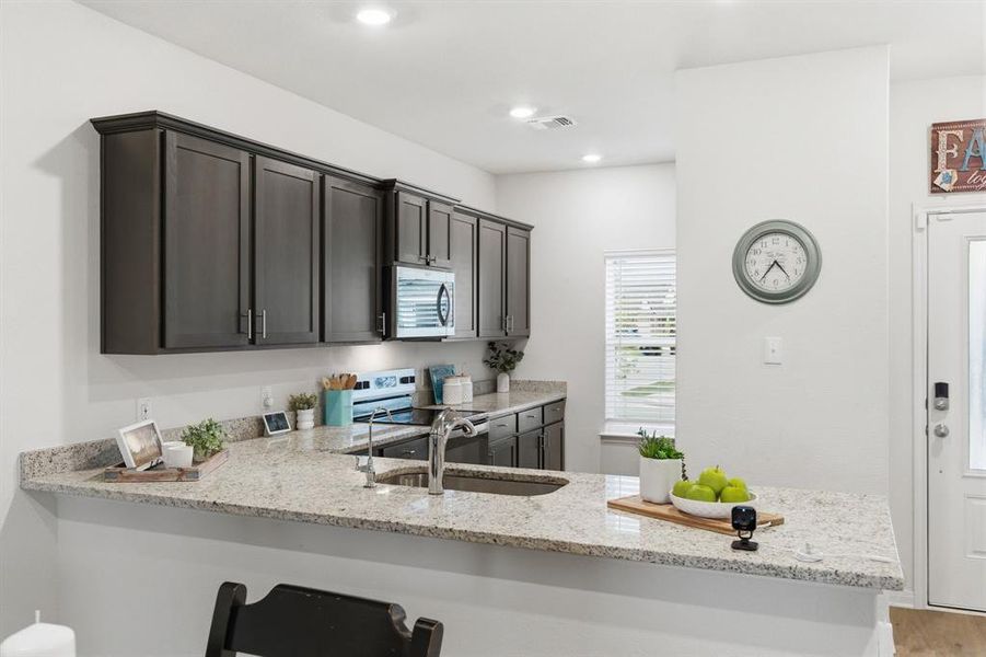 The kitchen features dark wood cabinetry, light granite countertops, a stainless steel microwave, and a stainless steel sink with a modern faucet