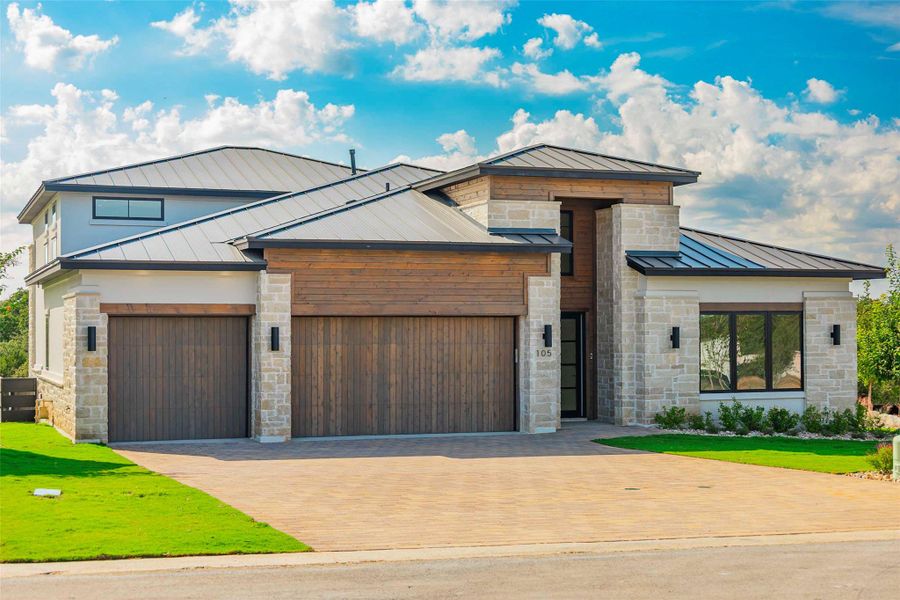 Modern home with a standing seam roof, a metal roof, stone siding, decorative driveway, and a garage
