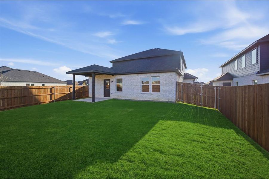 Expansive backyard featuring a manicured lawn, full privacy fencing, and a covered patio with a dark-framed roof