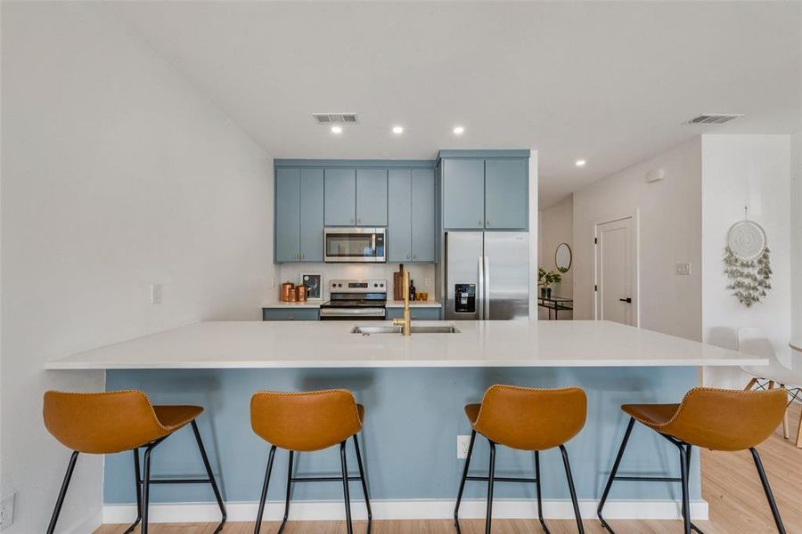 Kitchen with a breakfast bar area, sink, stainless steel appliances, and light hardwood / wood-style flooring