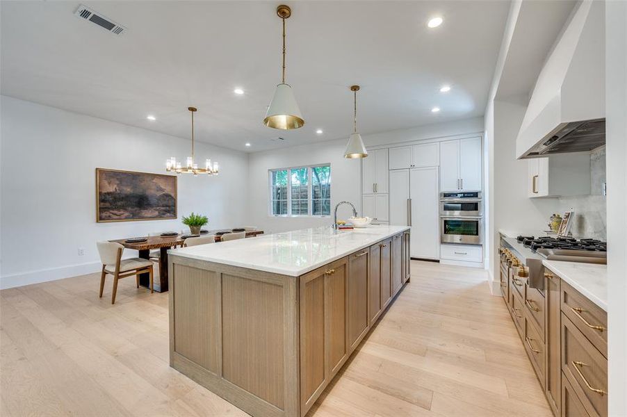 Kitchen with stainless steel appliances, wall chimney exhaust hood, light wood-style flooring, recessed lighting, and a large island