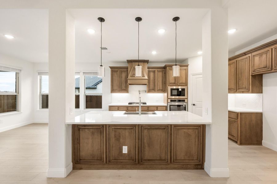 Kitchen with large island, white countertops, wood cabinets, pendant lights, and stainless steel appliances Kitchen with large island, white countertops, wood cabinets, pendant lights, and stainless steel appliances