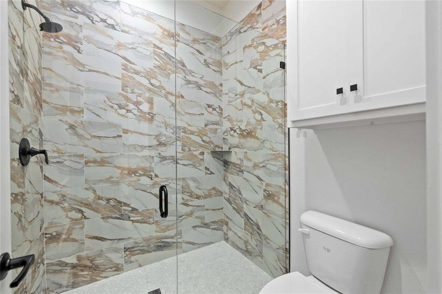 Full bath with a marble finish shower and toilet