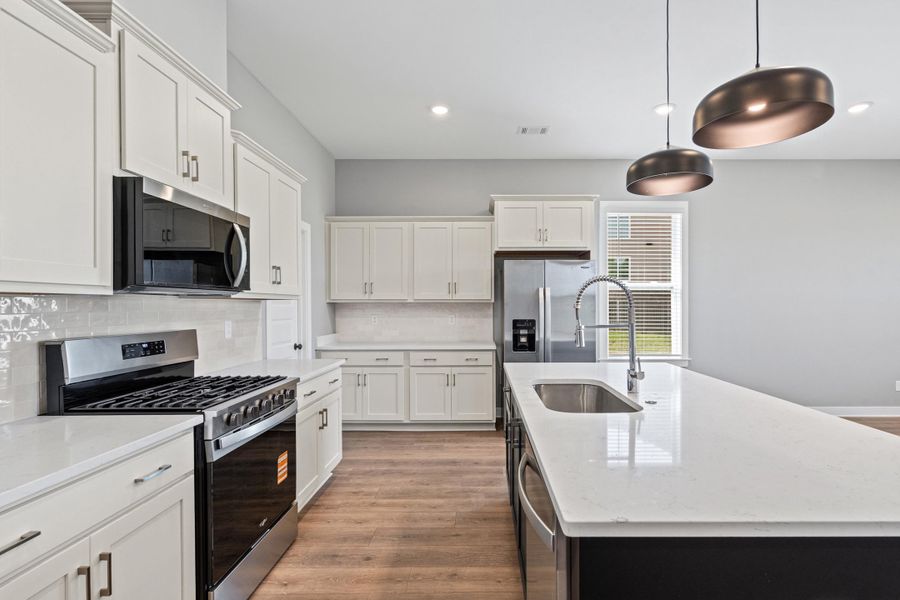 Kitchen featuring stainless steel appliances, light wood-style flooring, light stone counters, pendant lighting, and two tone cabinets