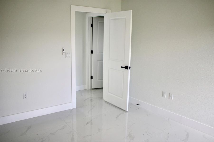Neutral-toned interior featuring large-format polished tile flooring, white two-panel interior doors, and matte black door hardware