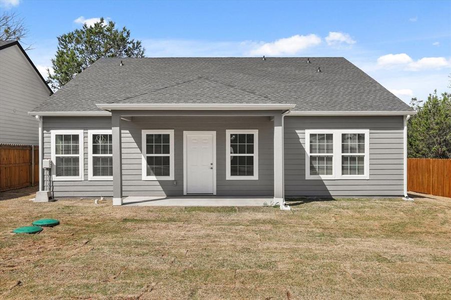 Rear view of house featuring a shingled roof, a lawn, a fenced backyard, and a patio area