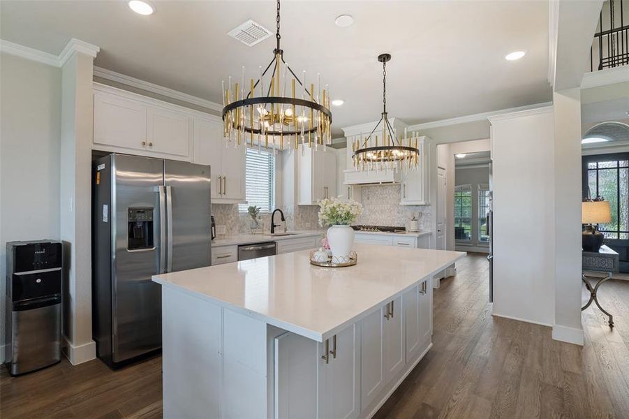 Spacious kitchen featuring an expansive central island with a white solid surface countertop, white shaker cabinetry, stainless steel appliances, and wood-finish flooring