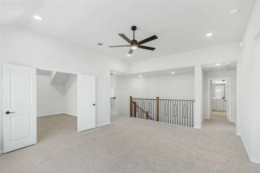 Spacious upstairs loft with carpet, ceiling fan, staircase railing, and open doorways to adjacent rooms