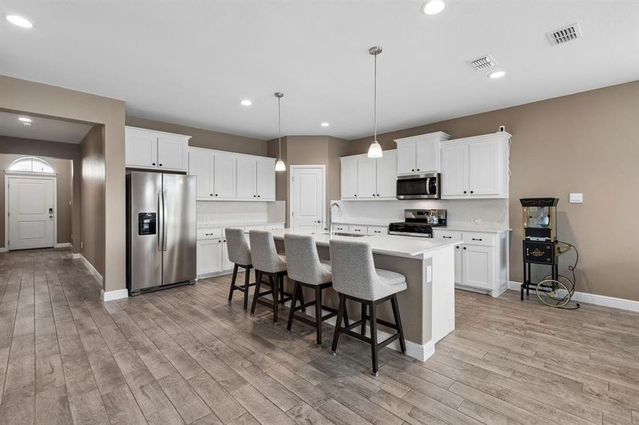 Modern kitchen featuring a central island with seating, white cabinetry, stainless steel appliances, and wood-finish flooring throughout