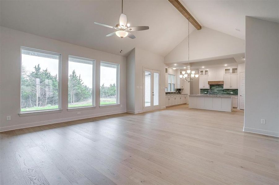 Unfurnished living room with a wealth of natural light, ceiling fan with notable chandelier, beam ceiling, and light hardwood / wood-style flooring