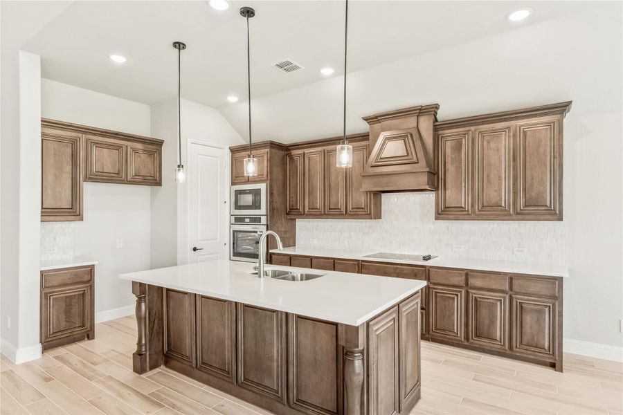 Kitchen with dark wood cabinets, large center island with sink, white countertops, and pendant lights overhead Kitchen with dark wood cabinets, large center island with sink, white countertops, and pendant lights overhead