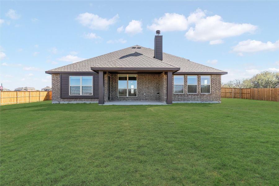 Rear view of single-story brick home with covered patio, chimney, and fenced backyard lawn Rear view of single-story brick home with covered patio, chimney, and fenced backyard lawn