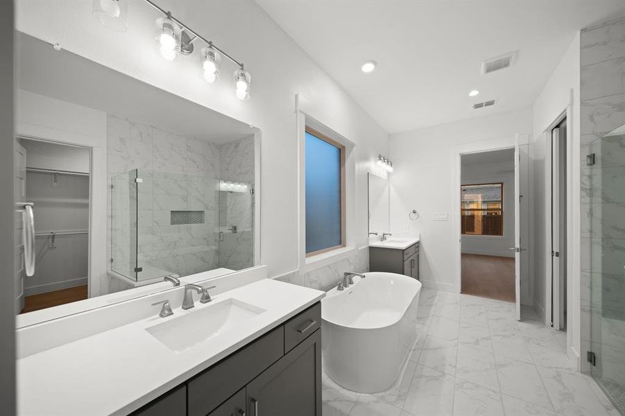 Full bathroom with light marble finish flooring, two vanities, a spacious closet, a freestanding tub, and a marble finish shower