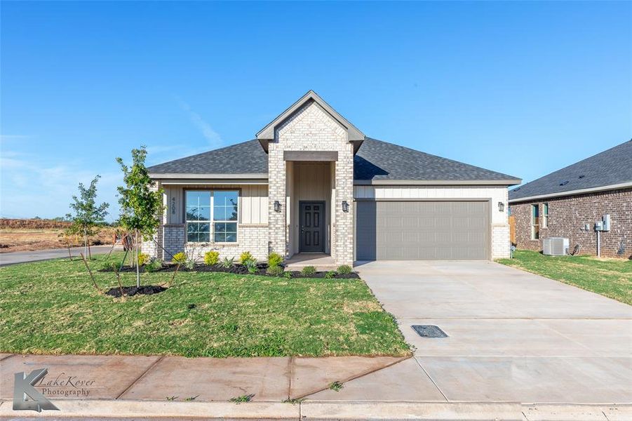 View of front facade with concrete driveway, brick siding, a shingled roof, a front yard, and an attached garage