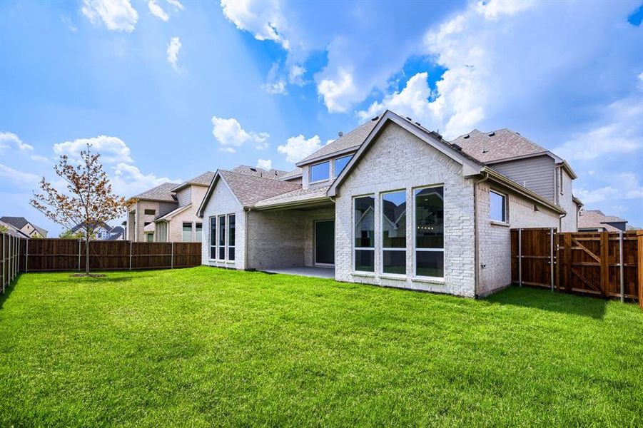 Spacious backyard featuring a manicured lawn, a young tree, and a covered patio Spacious backyard featuring a manicured lawn, a young tree, and a covered patio