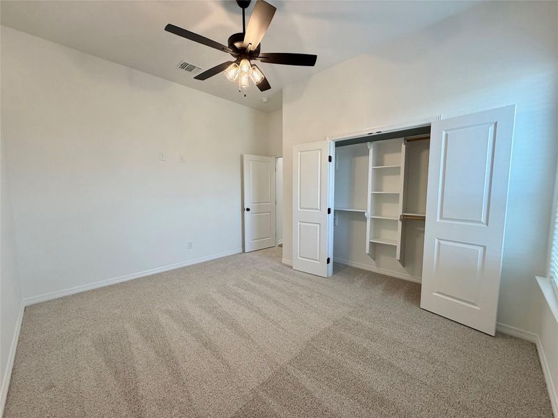 Room featuring vaulted ceilings, neutral-toned carpeting, a ceiling fan with integrated lighting, and a closet with bifold doors and built-in shelving