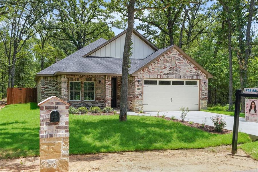 Brick and stone facade residence featuring a dark shingle roof, a two-car garage, and a manicured lawn Brick and stone facade residence featuring a dark shingle roof, a two-car garage, and a manicured lawn