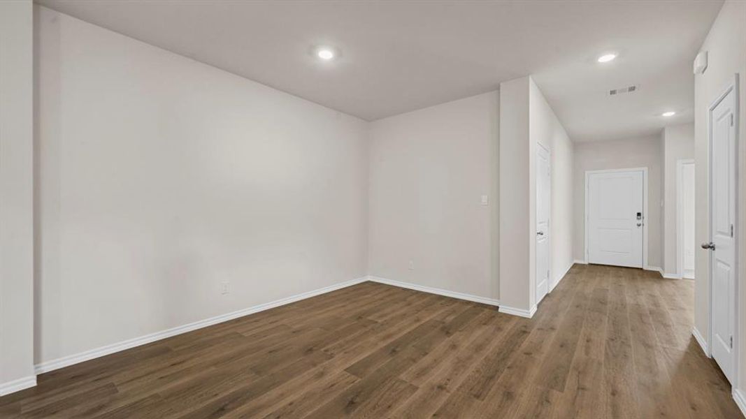 Spacious room with wood-finish flooring, recessed lighting, and crisp white baseboards, offering a versatile layout Spacious room with wood-finish flooring, recessed lighting, and crisp white baseboards, offering a versatile layout