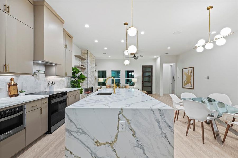 Kitchen featuring black electric range oven, sink, oven, hanging light fixtures, and a center island with sink