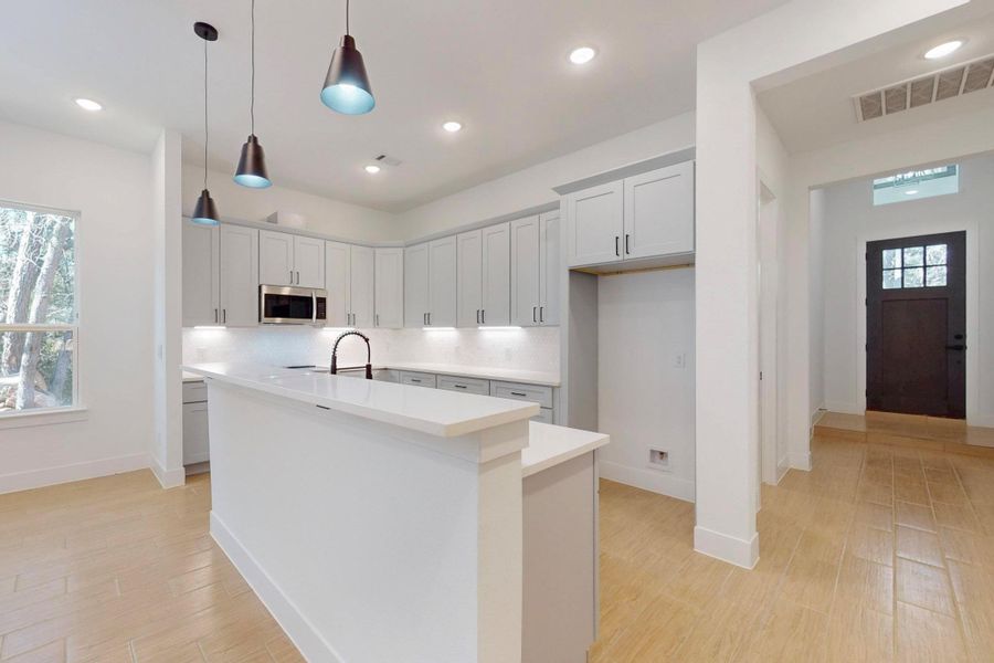 Kitchen with a kitchen island with sink, white cabinets, hanging light fixtures, and light wood-type flooring
