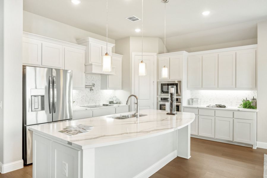 White kitchen with large curved island, quartz countertops, pendant lights, and stainless steel appliances White kitchen with large curved island, quartz countertops, pendant lights, and stainless steel appliances