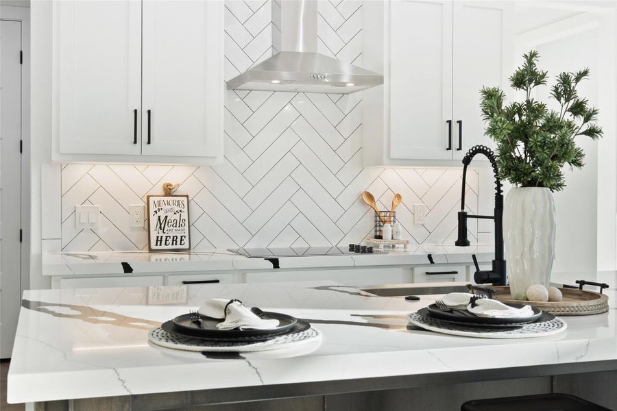 Kitchen featuring wall chimney range hood, white cabinetry, light stone countertops, and tasteful backsplash
