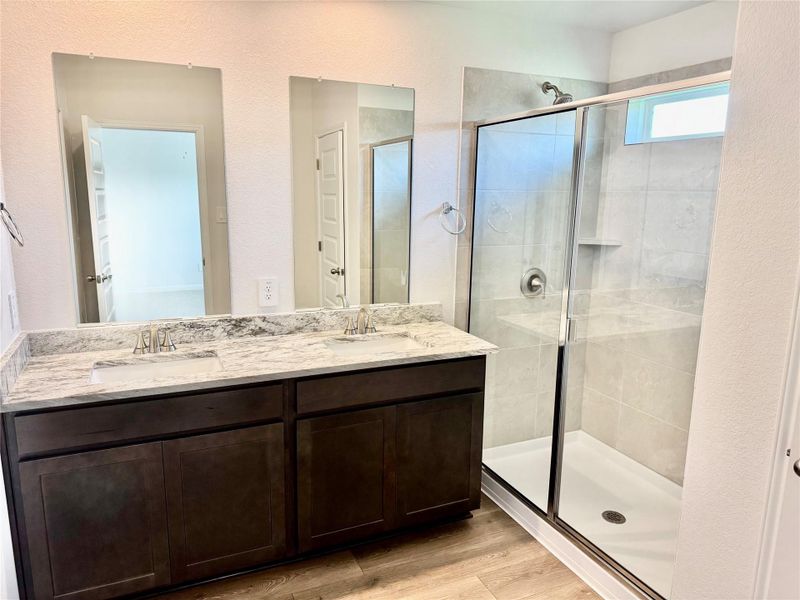 Bathroom featuring a stall shower, wood finished floors, double vanity, and a textured wall Bathroom featuring a stall shower, wood finished floors, double vanity, and a textured wall