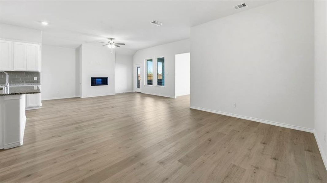 Unfurnished living room featuring light wood finished floors, ceiling fan, and a glass covered fireplace