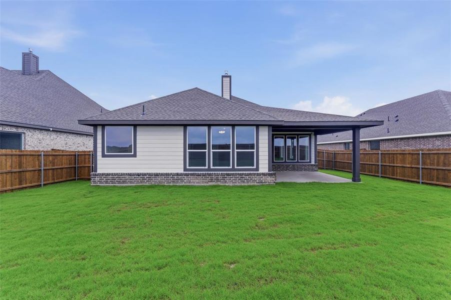 Expansive grassy yard with a privacy fence, featuring a covered patio, brick foundation, light-colored siding, and large windows