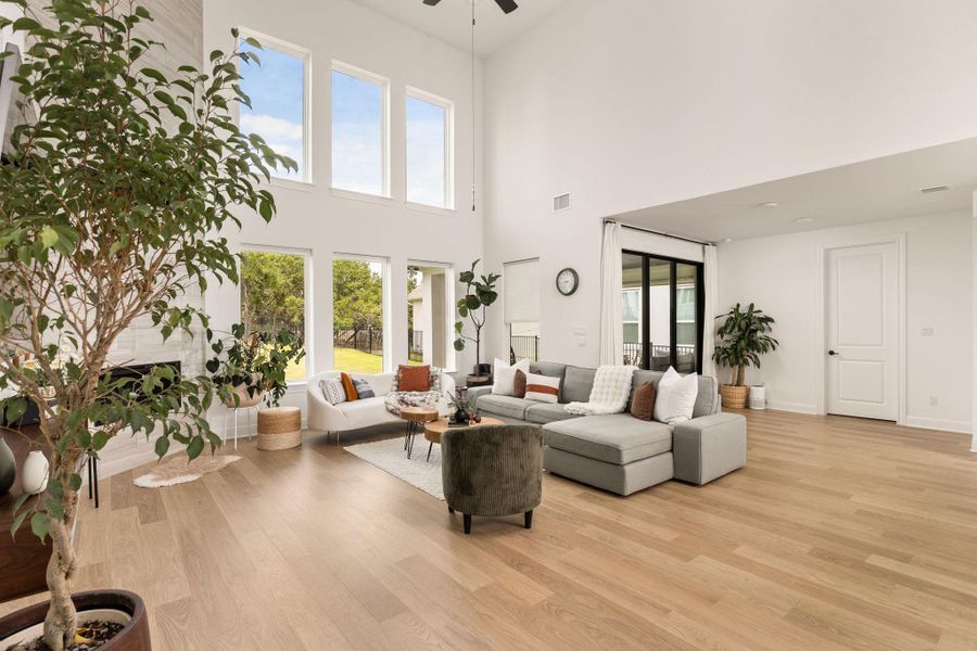Spacious living area featuring high vaulted ceilings, expansive window array, light wood-finish flooring, a white brick-style fireplace, and an exterior sliding glass door