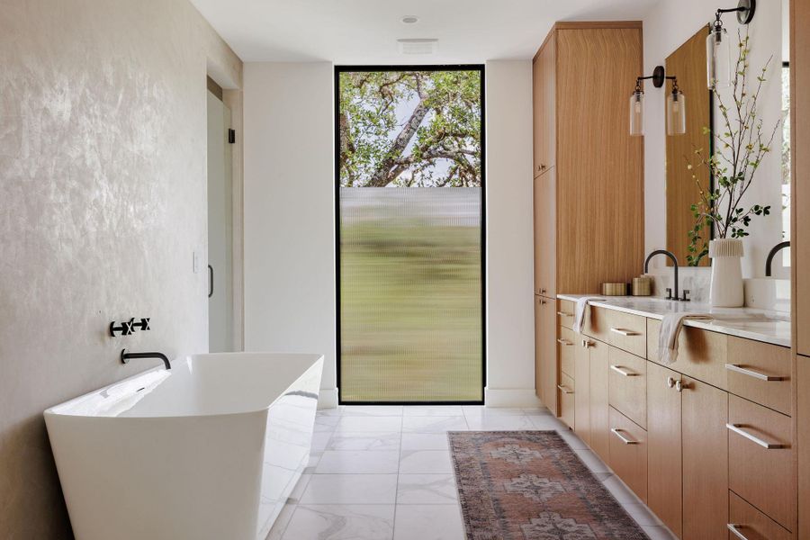 Bathroom featuring double vanity, a freestanding tub, marble finish floors, and a wall of windows Bathroom featuring double vanity, a freestanding tub, marble finish floors, and a wall of windows