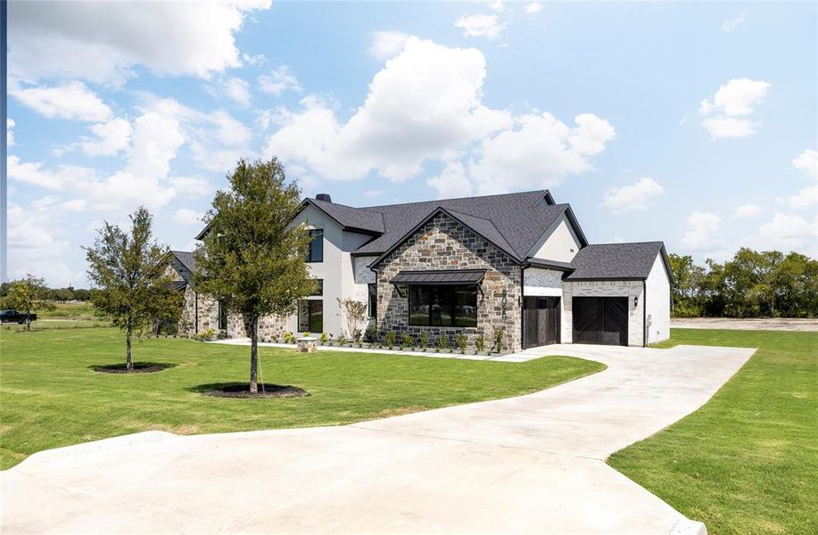 View of front of home with stone siding, a front lawn, driveway, a shingled roof, and stucco siding