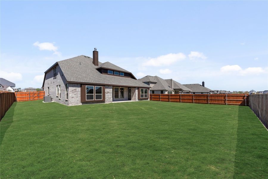 Rear view of brick home with large grassy backyard enclosed by wood privacy fence Rear view of brick home with large grassy backyard enclosed by wood privacy fence