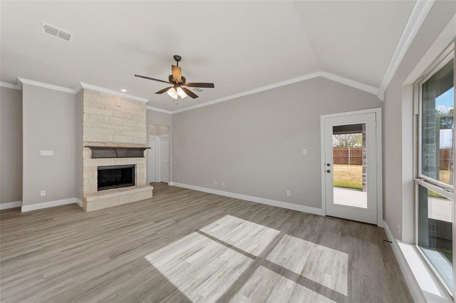 Unfurnished living room with plenty of natural light, light hardwood / wood-style floors, crown molding, and a fireplace