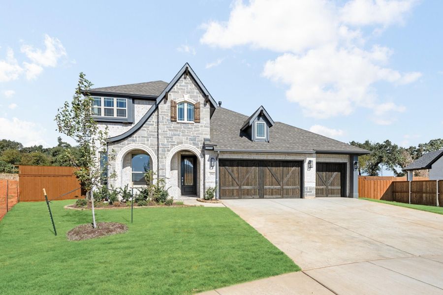 Two-story stone and brick home with arched entry, wood garage doors, and manicured front lawn