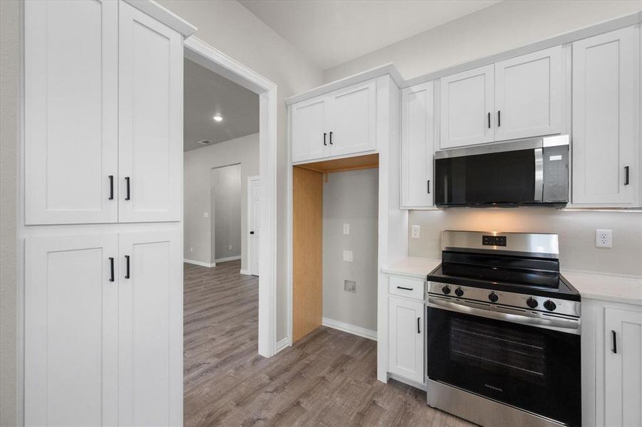 Modern kitchen featuring white shaker cabinetry, stainless steel range and microwave, white countertops, and wood-finish flooring