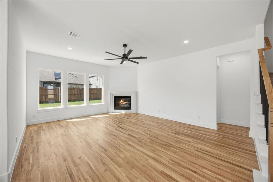 Unfurnished living room with a warm lit fireplace, light wood-style floors, ceiling fan, and recessed lighting
