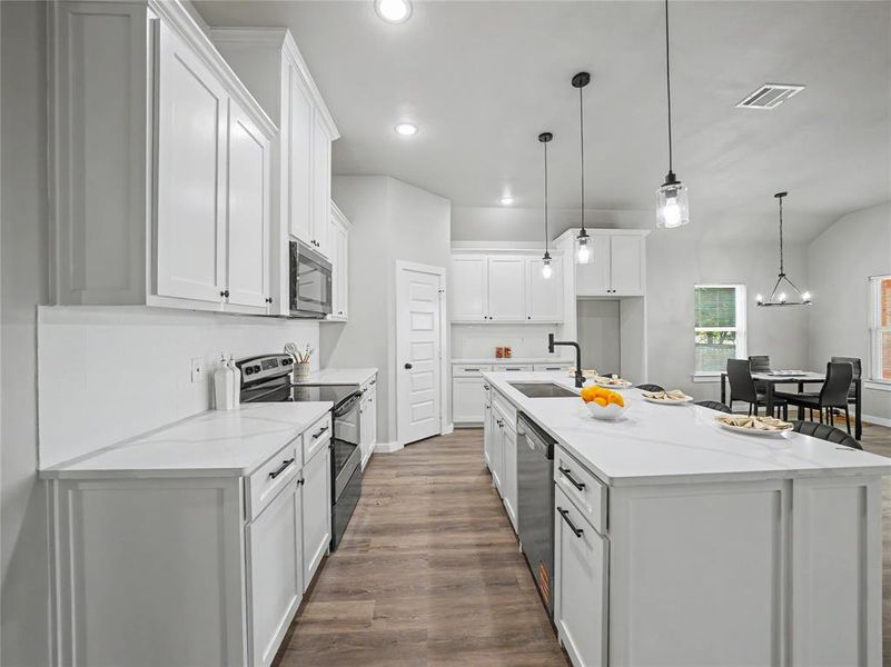 Open-concept kitchen featuring white shaker cabinetry, an expansive center island with seating, quartz countertops, stainless steel appliances, and wood-finish flooring Open-concept kitchen featuring white shaker cabinetry, an expansive center island with seating, quartz countertops, stainless steel appliances, and wood-finish flooring
