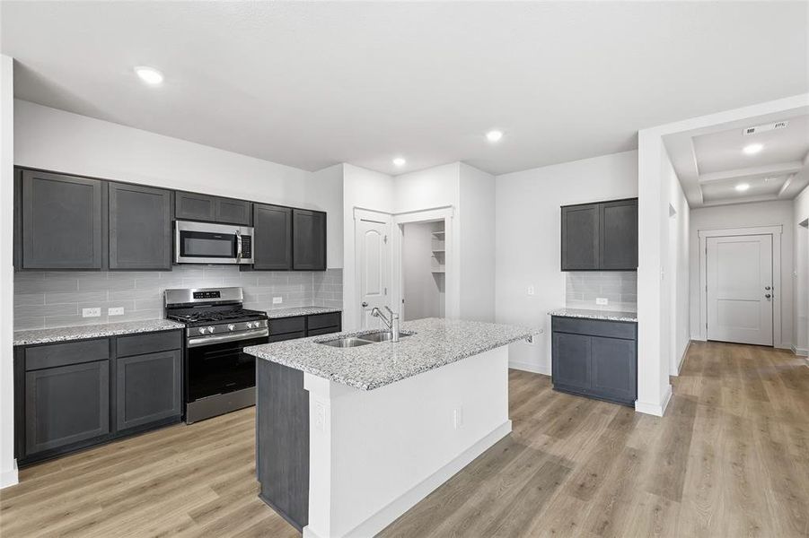 Kitchen featuring stainless steel appliances, backsplash, light stone counters, light wood finished floors, and recessed lighting