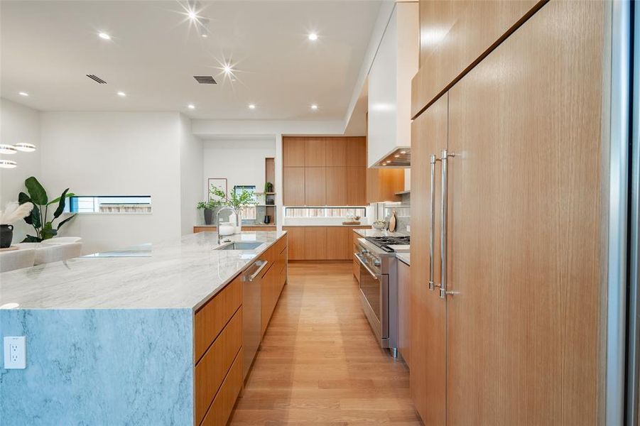 Kitchen with a spacious island, sink, high end appliances, light stone countertops, and light hardwood / wood-style floors