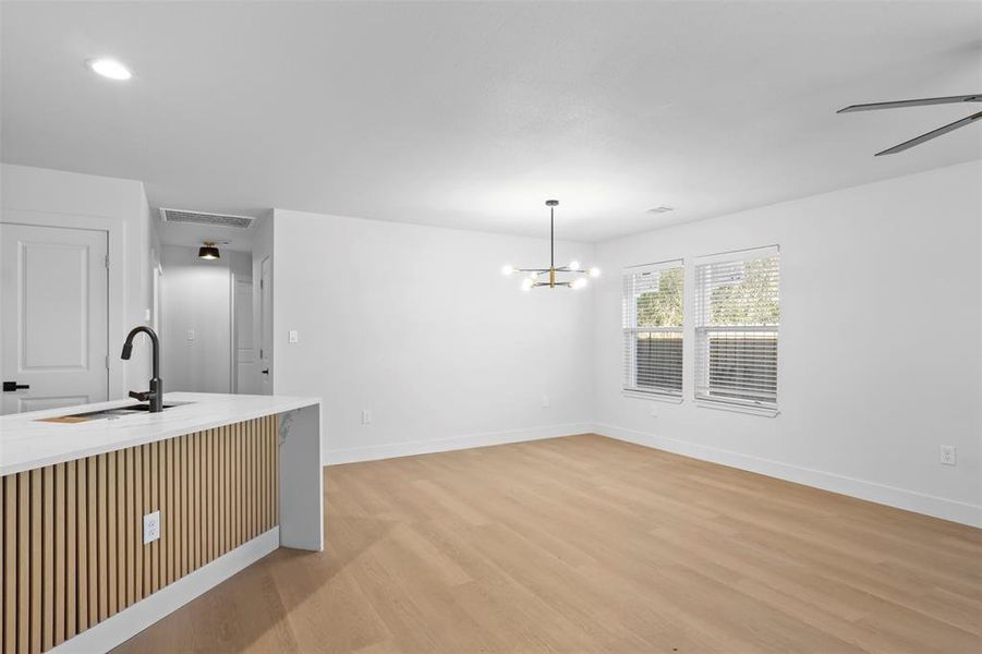 Kitchen with sink, hanging light fixtures, light wood-type flooring, and ceiling fan with notable chandelier