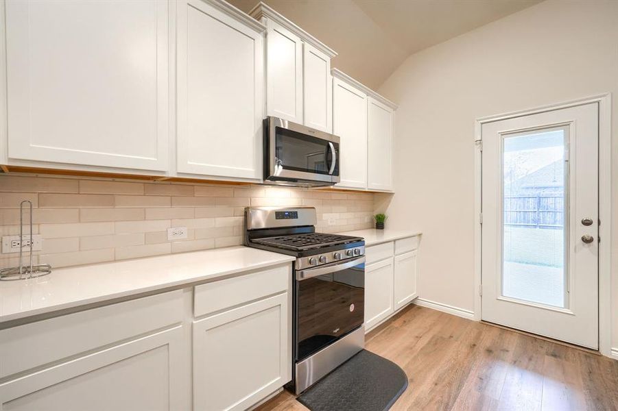 Kitchen featuring appliances with stainless steel finishes, white cabinets, lofted ceiling, light wood-style flooring, and tasteful backsplash Kitchen featuring appliances with stainless steel finishes, white cabinets, lofted ceiling, light wood-style flooring, and tasteful backsplash