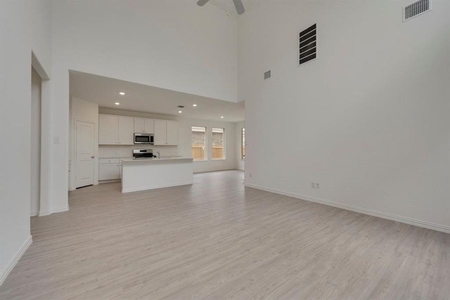 Unfurnished living room featuring a towering ceiling, light wood-type flooring, and ceiling fan