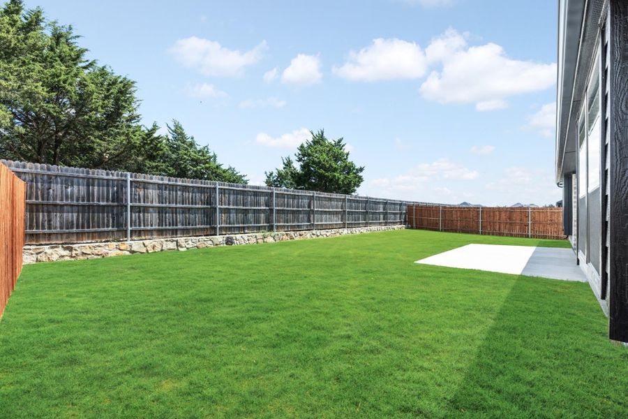 Spacious backyard with green lawn, concrete patio, and wood privacy fence along stone retaining wall